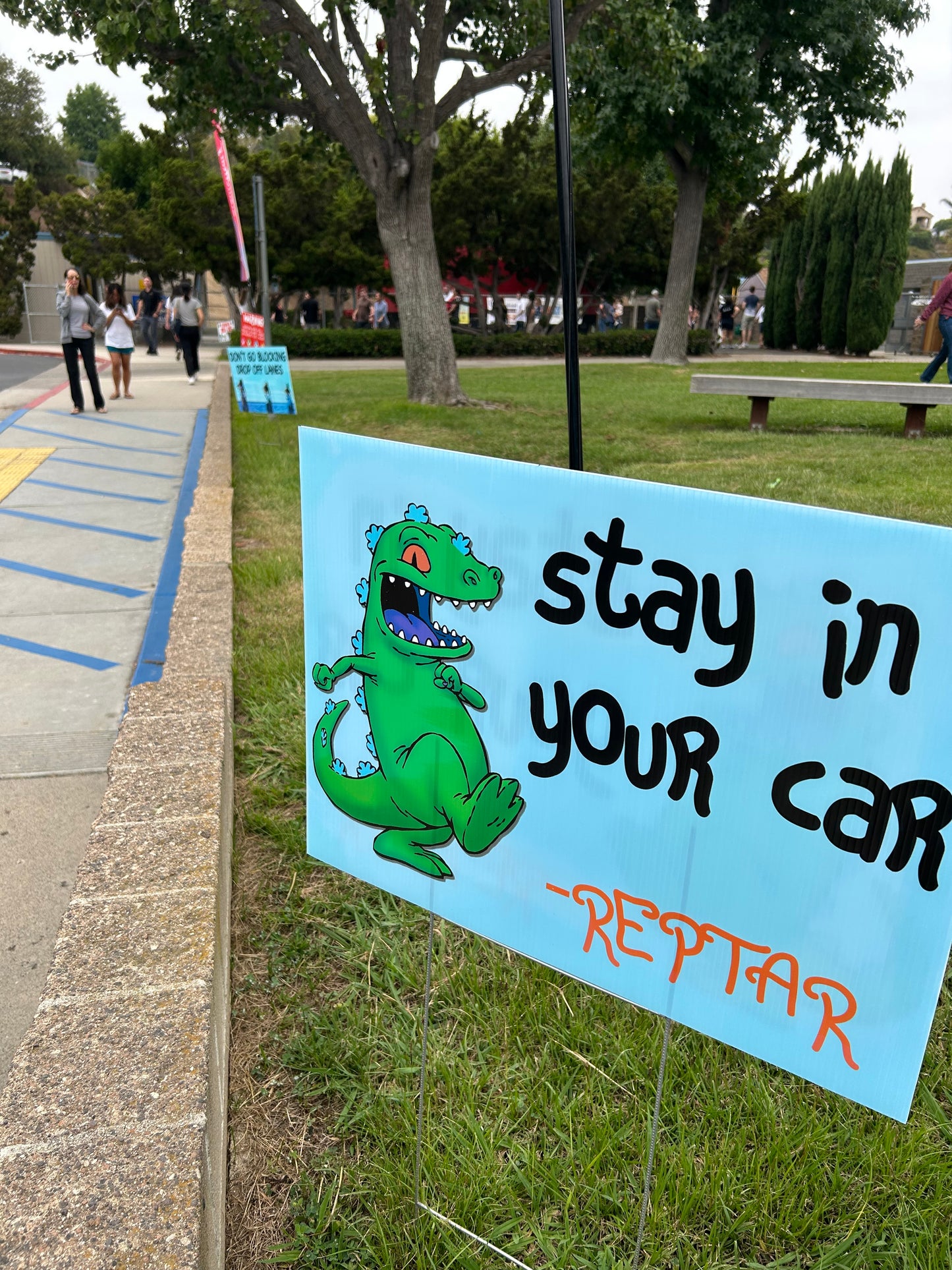 Sign with cartoon alligator and text 'Stay in your car REPTAR' on a grassy background