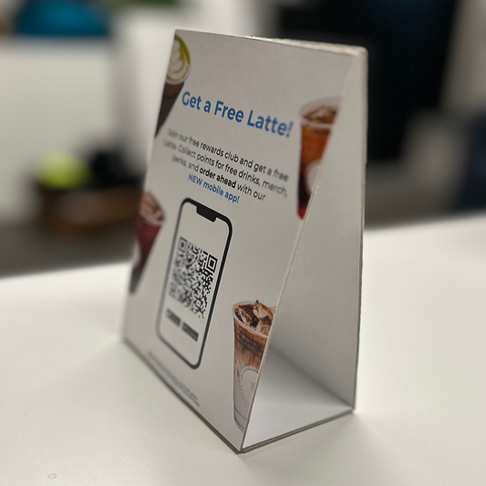 Promotional sign with QR code for a free latté at a coffee shop, placed on a counter.