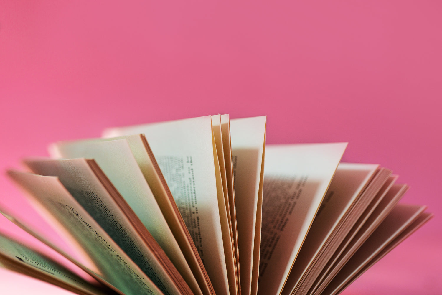 Close-up of a book being fanned open, with pages slightly separated to reveal text and details. This image conveys a sense of curiosity and learning, perfect for illustrating reading, literature, or educational themes in a warm, inviting setting.