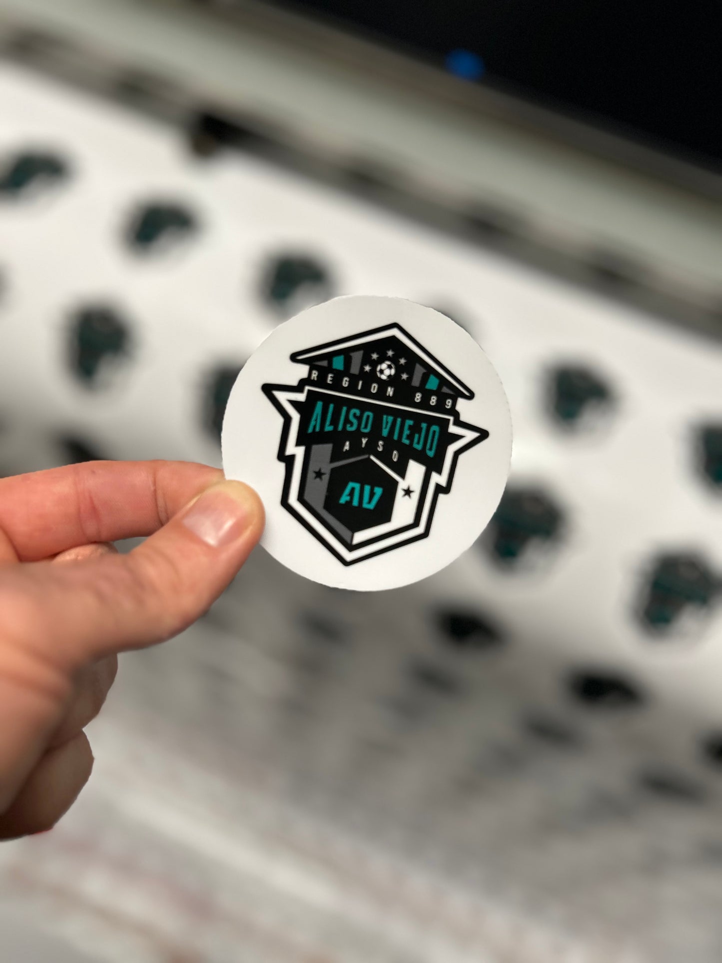 Hand holding a sticker with a logo and text, blurred background