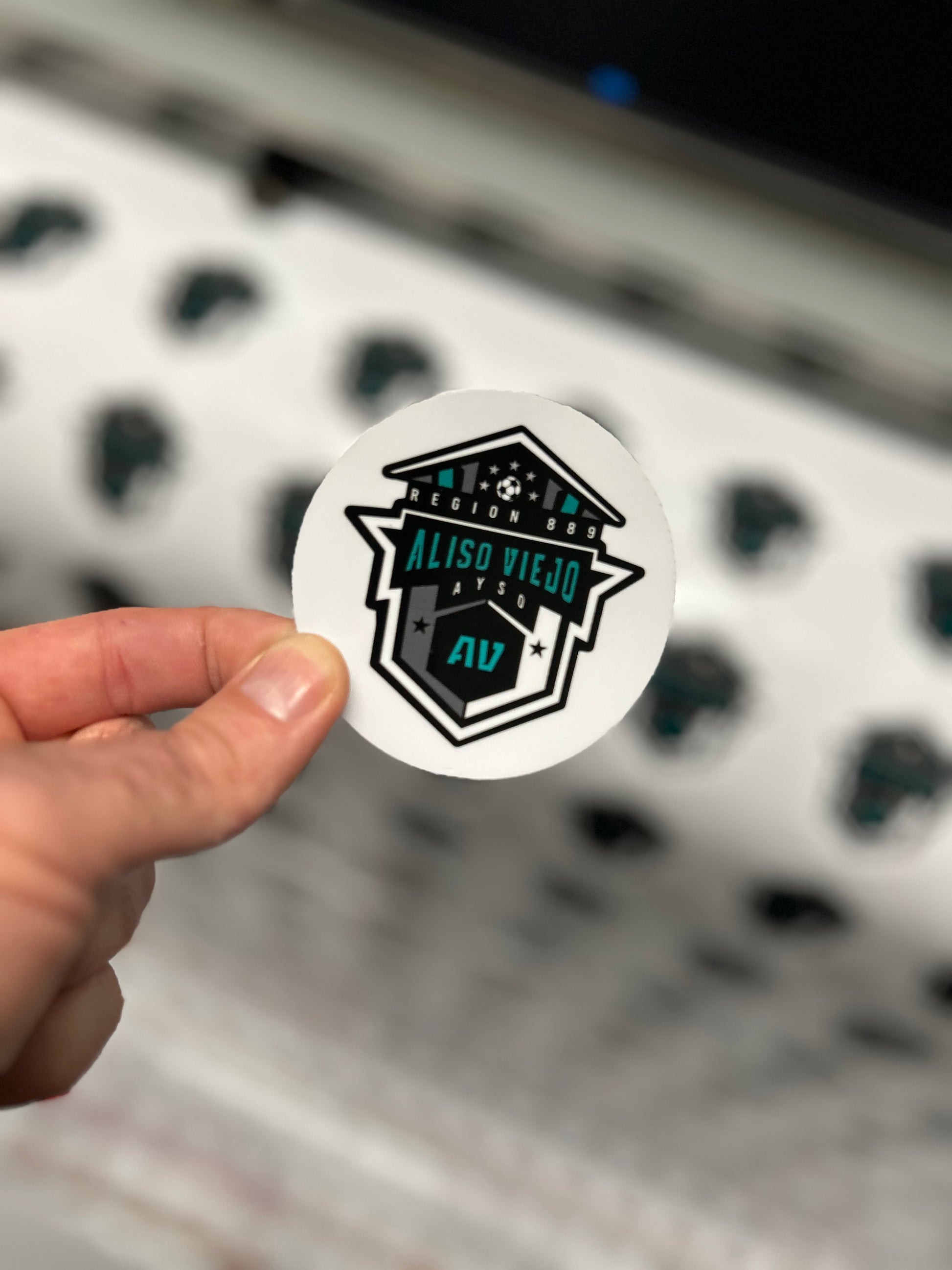 Hand holding a sticker with a logo and text, blurred background