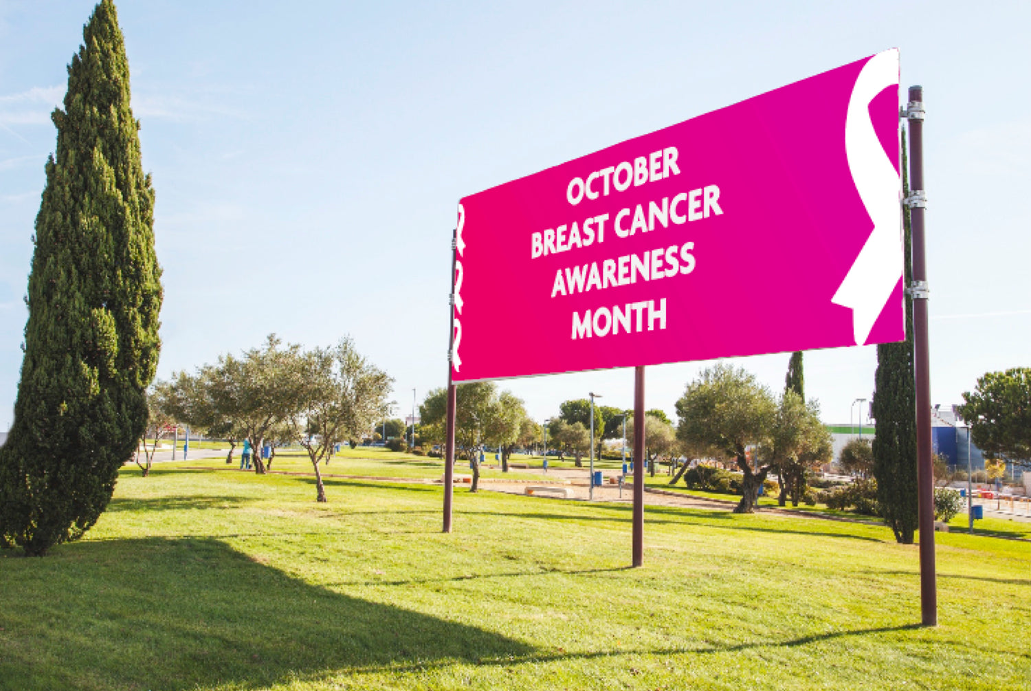 Pink banner with 'October Breast Cancer Awareness Month' text on a grassy area with trees and buildings in the background.
