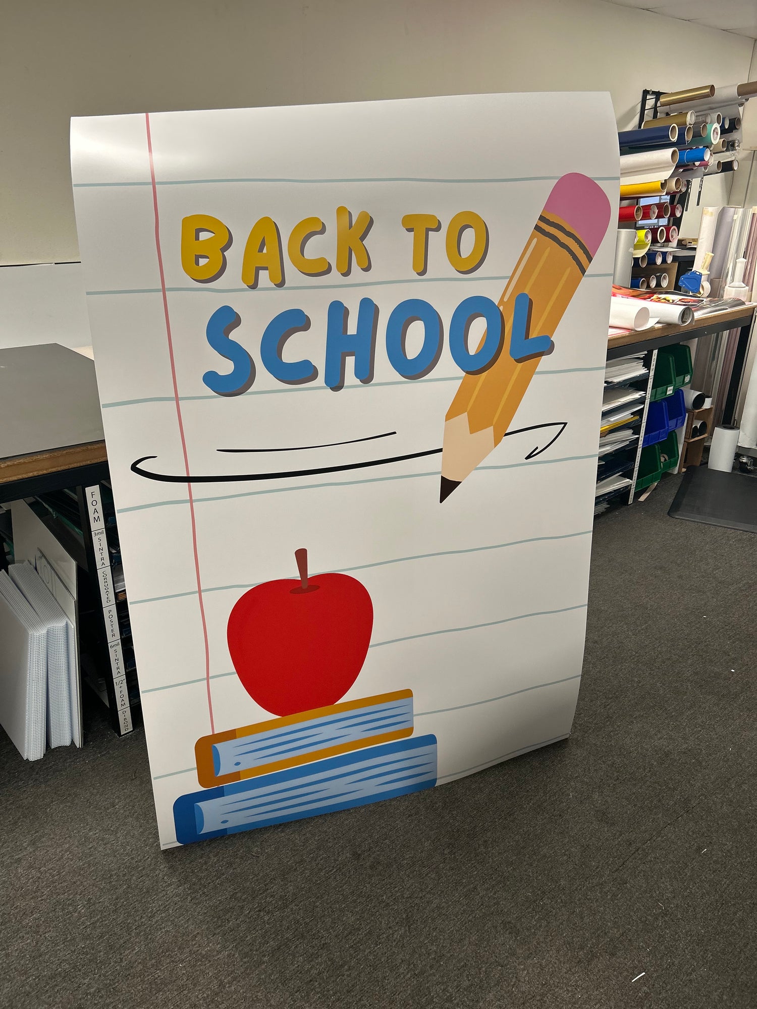 Cardboard sign with 'Back to School' text and graphics on a gray floor.