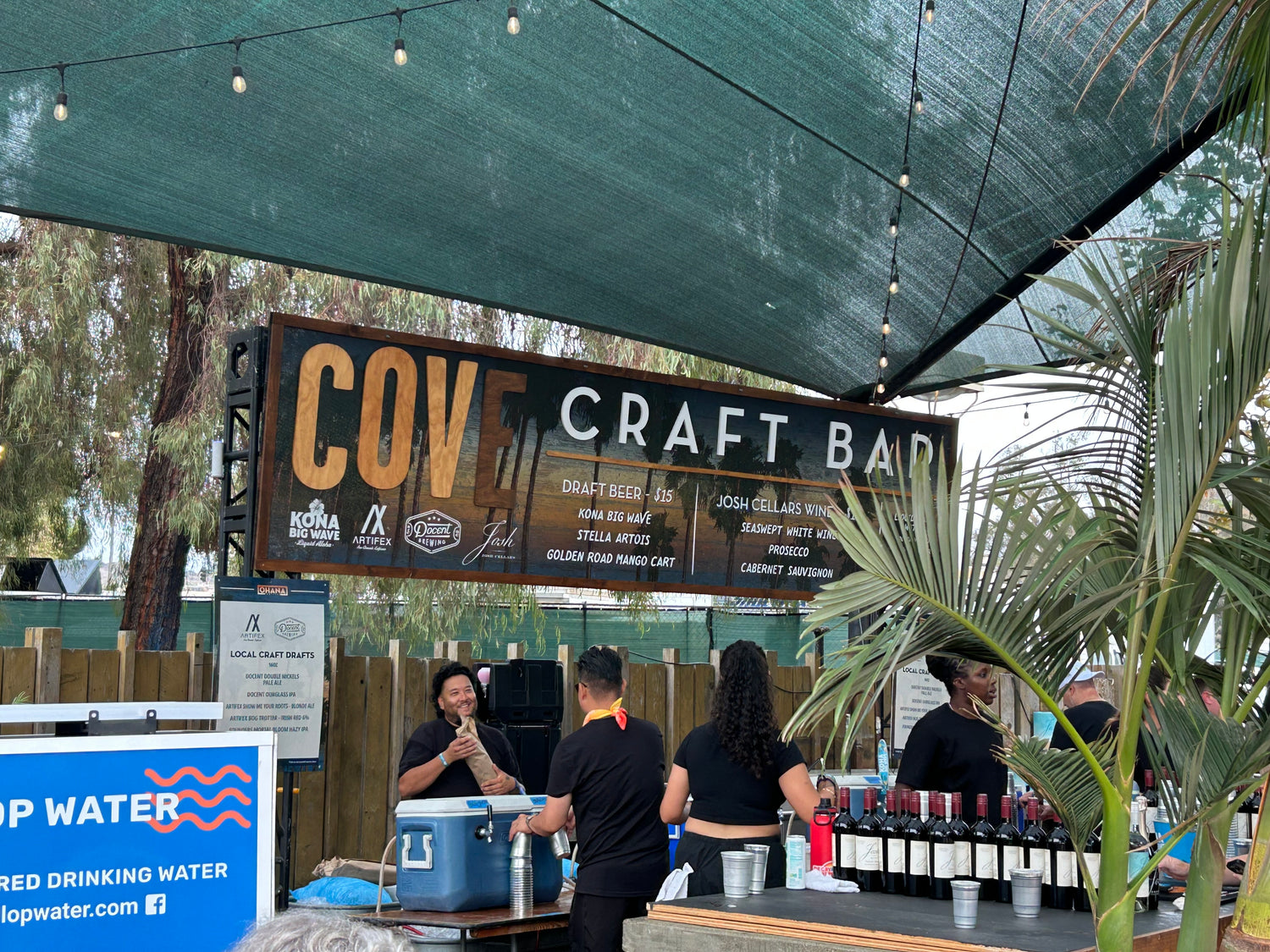 Outdoor setting with 'COV Craft Bar' sign and people around a table with bottles.