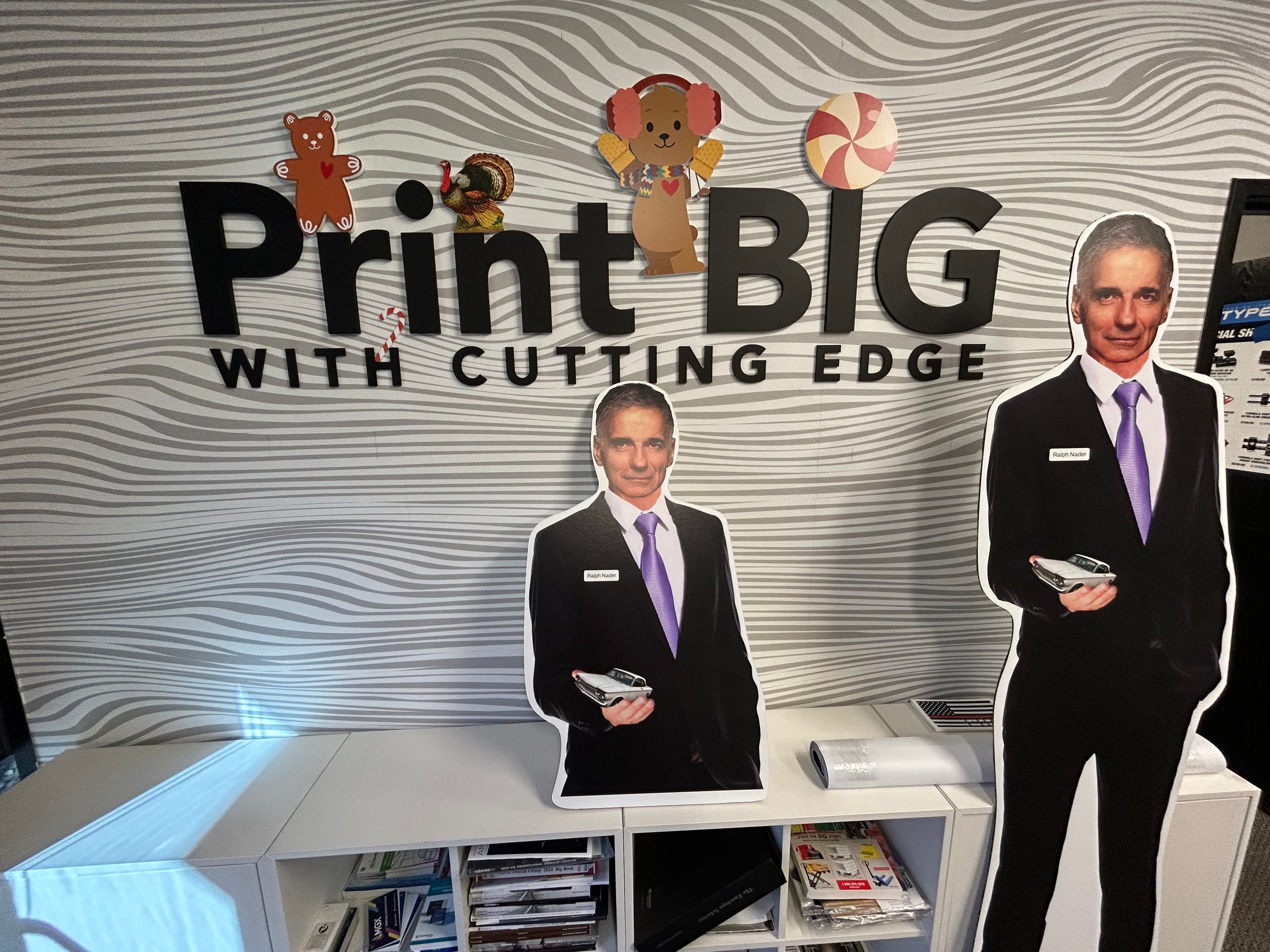 Cardboard cutouts of two men in suits with a promotional backdrop for 'Print Big with Cutting Edge'.