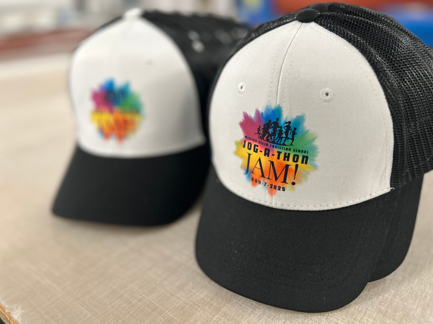 Two baseball caps with colorful logos on a cardboard surface