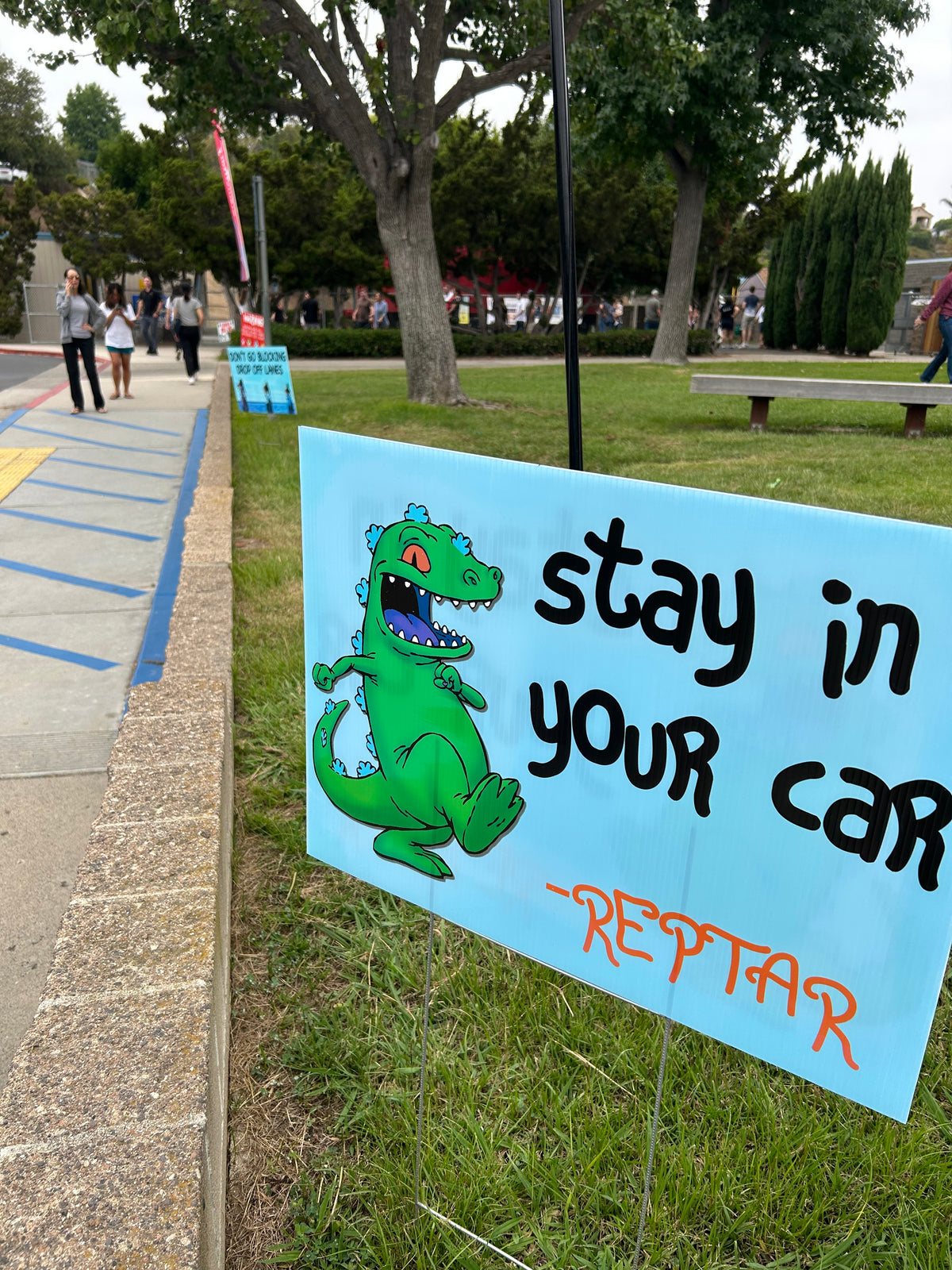 Sign with cartoon alligator and text 'Stay in your car REPTAR' on a grassy background
