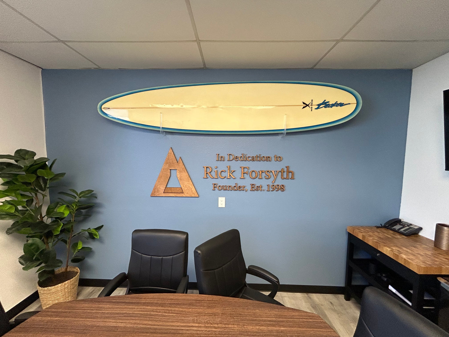 Office interior with a surfboard on the wall, dedication plaque, and office furniture.