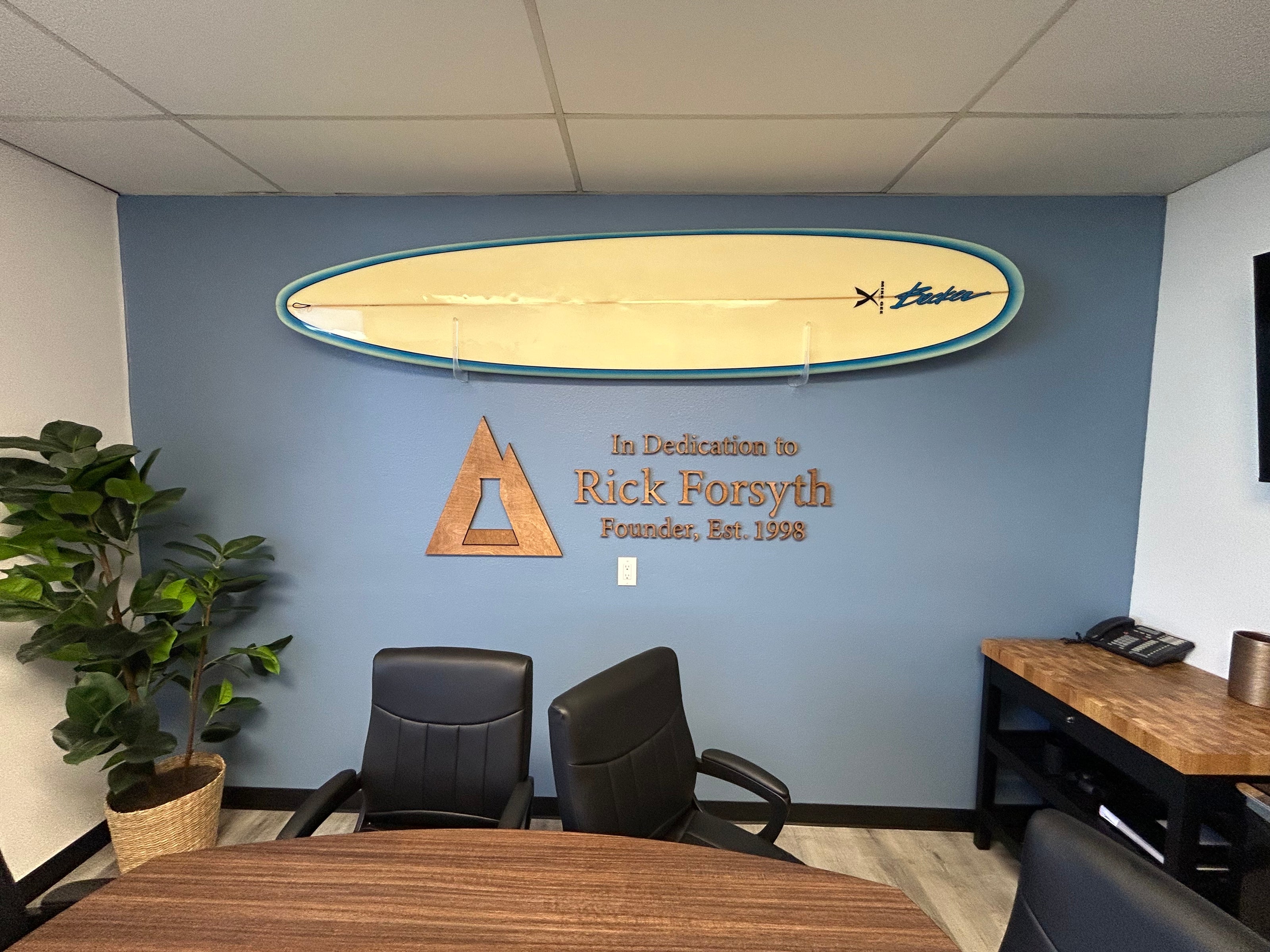 Office interior with a surfboard on the wall, dedication plaque, and office furniture.
