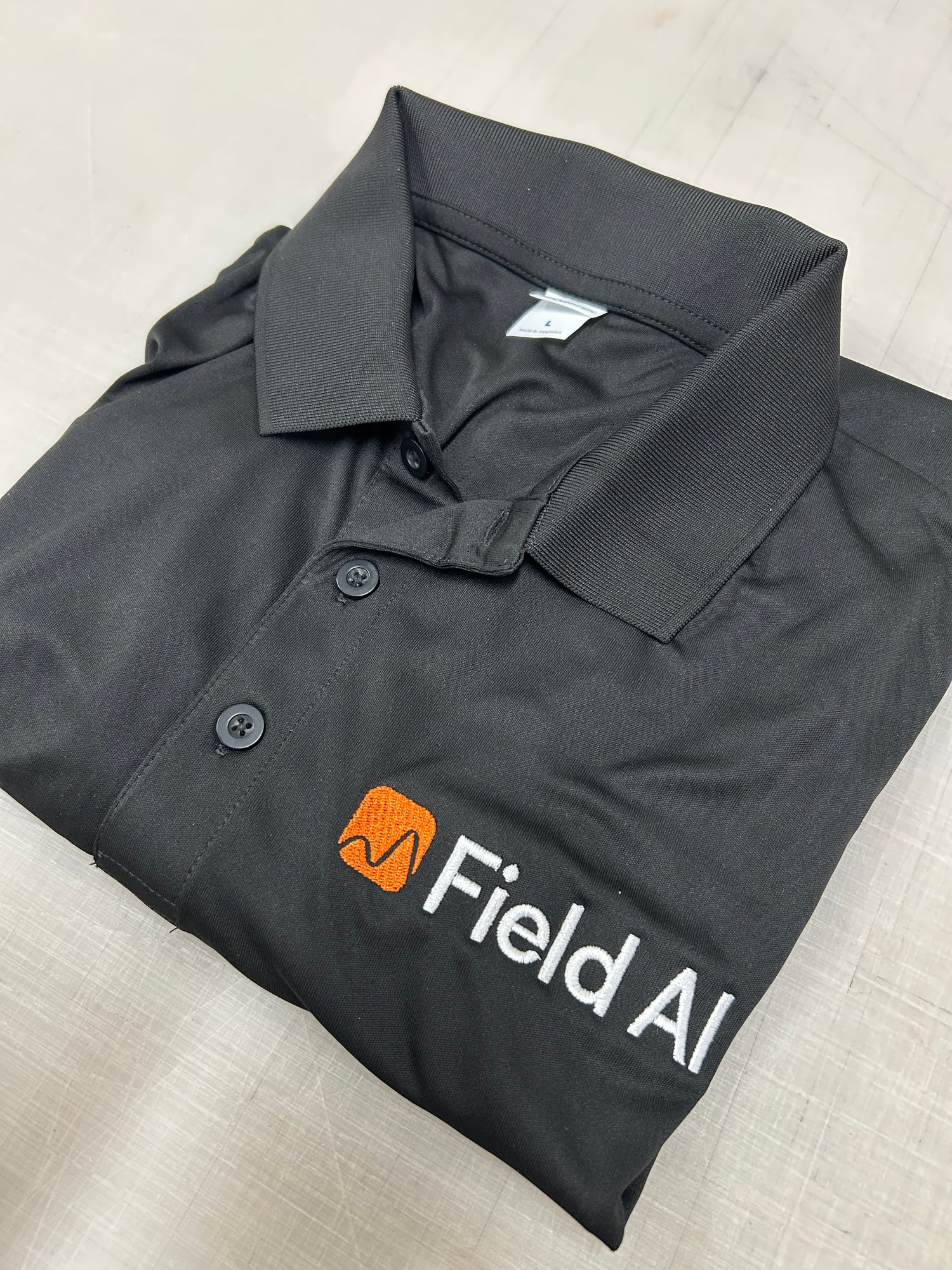 Black shirt with Field AI logo on a light gray surface