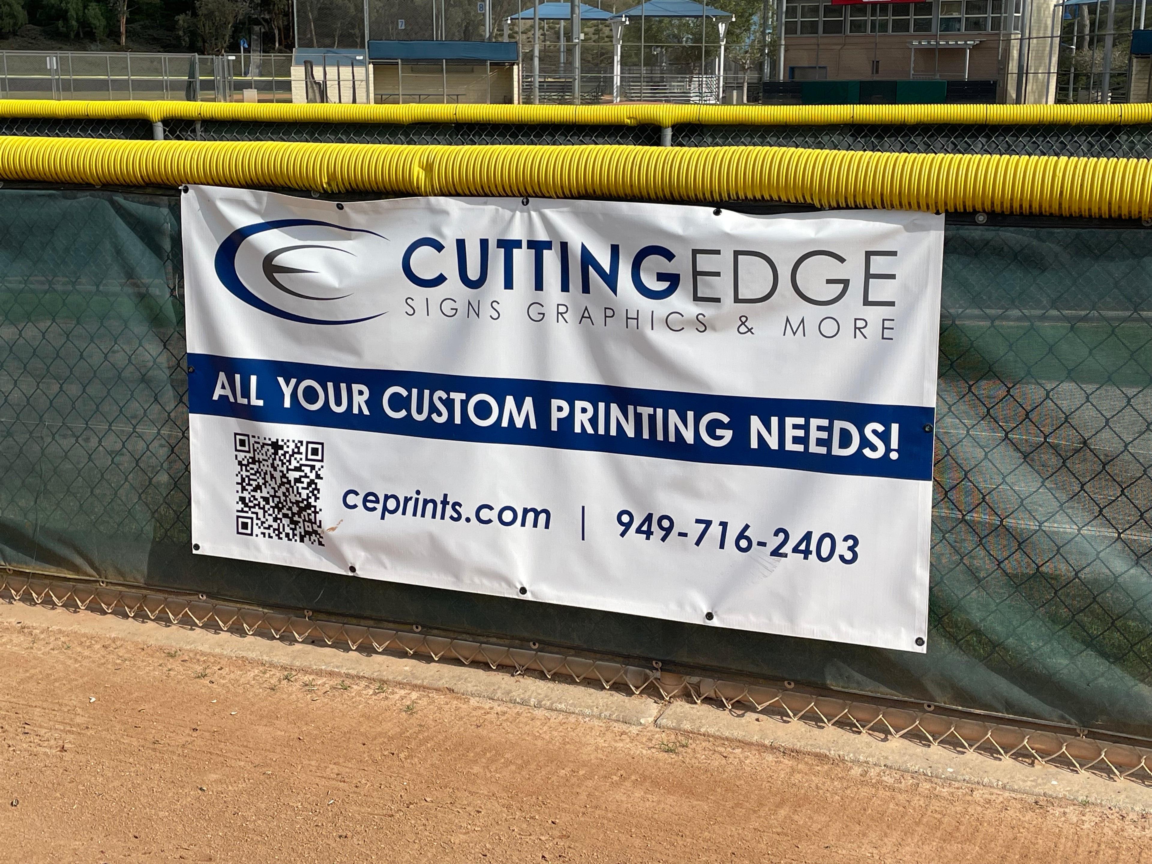 Cutting Edge Signs Graphics & More banner on a chain-link fence with a sports field background.