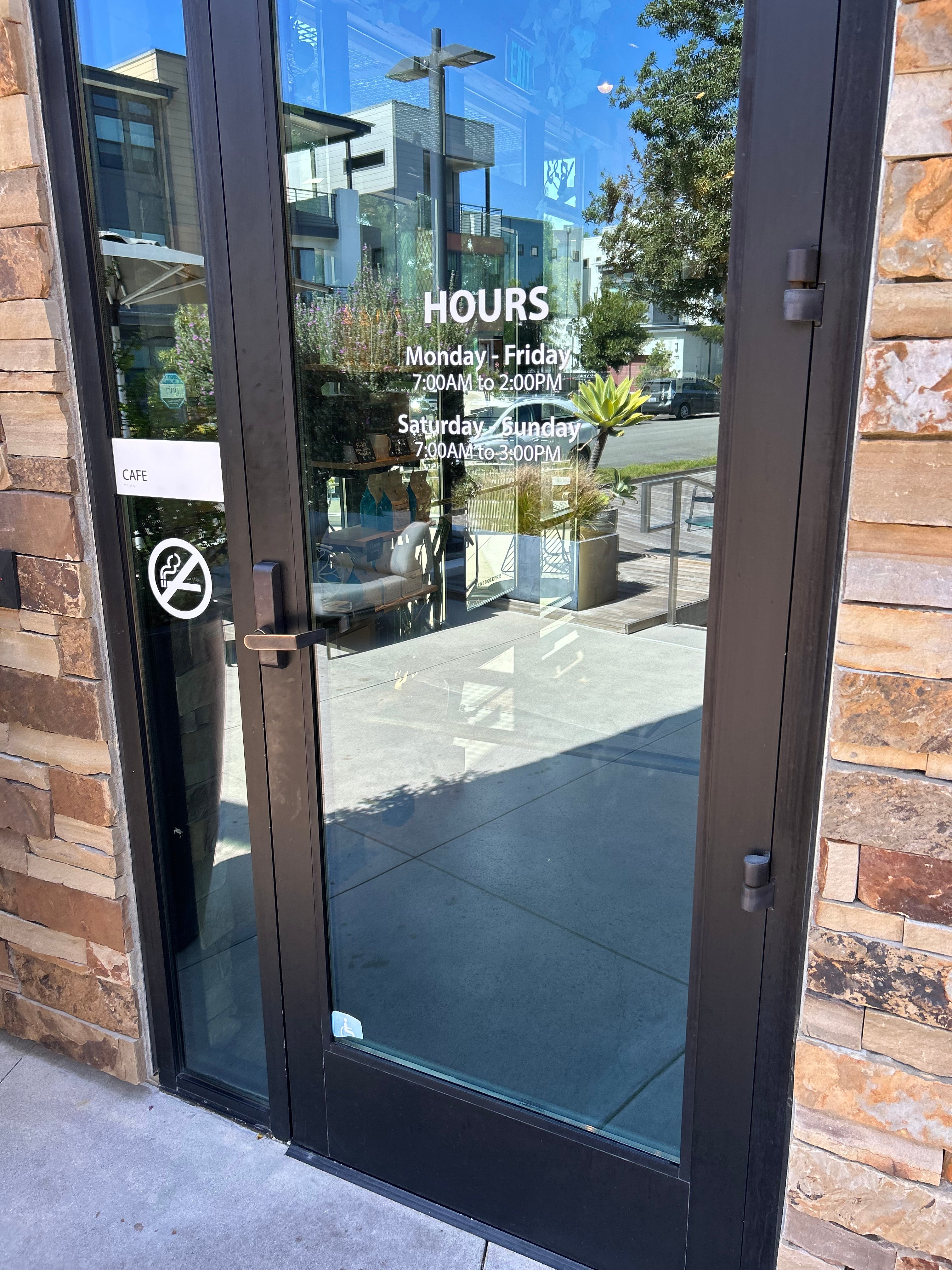 Glass door with reflections of a building and trees on a stone wall.