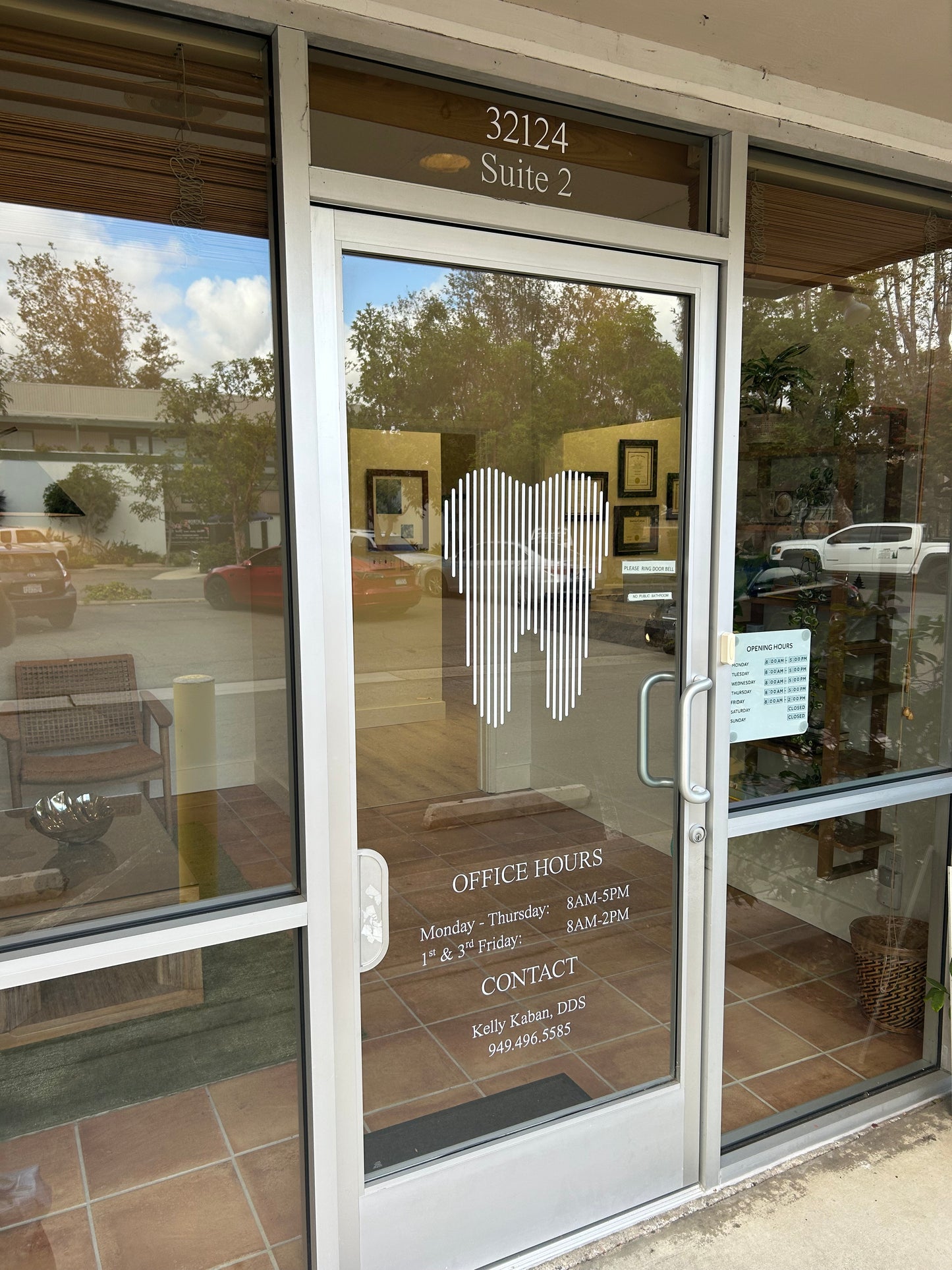 Glass door with reflections of trees and sky, featuring office hours and contact information.