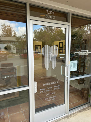 Glass door with reflections of trees and sky, featuring office hours and contact information.