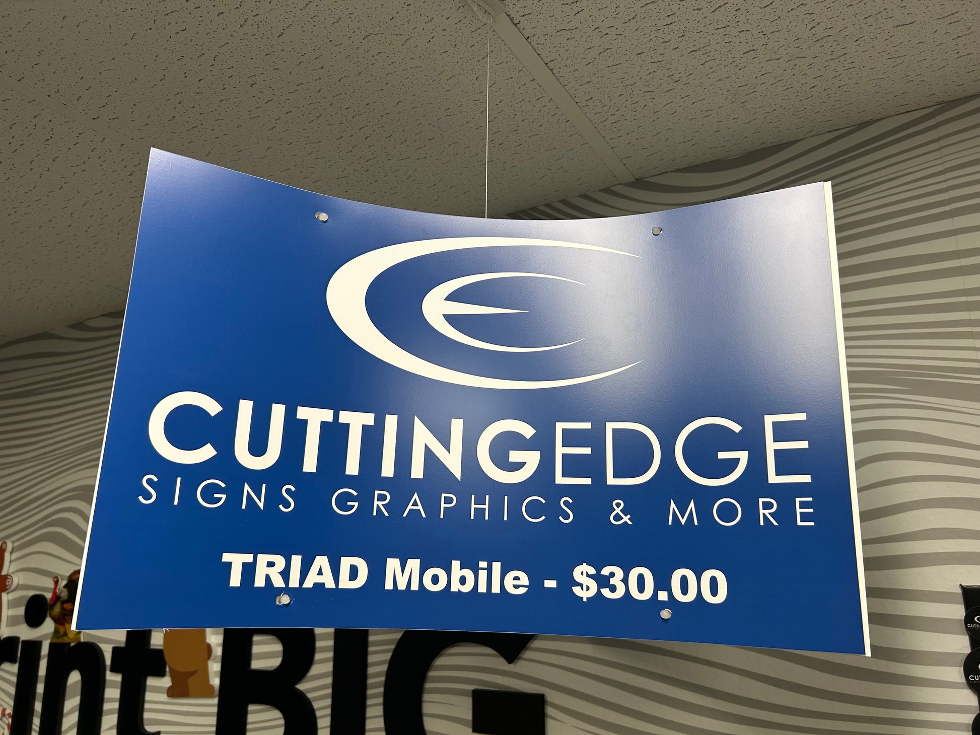 A custom ceiling mobile kit with a blue sign that reads 'CUTTING EDGE SIGNS GRAPHICS & MORE TRIAD Mobile - $30.00' suspended from the ceiling.