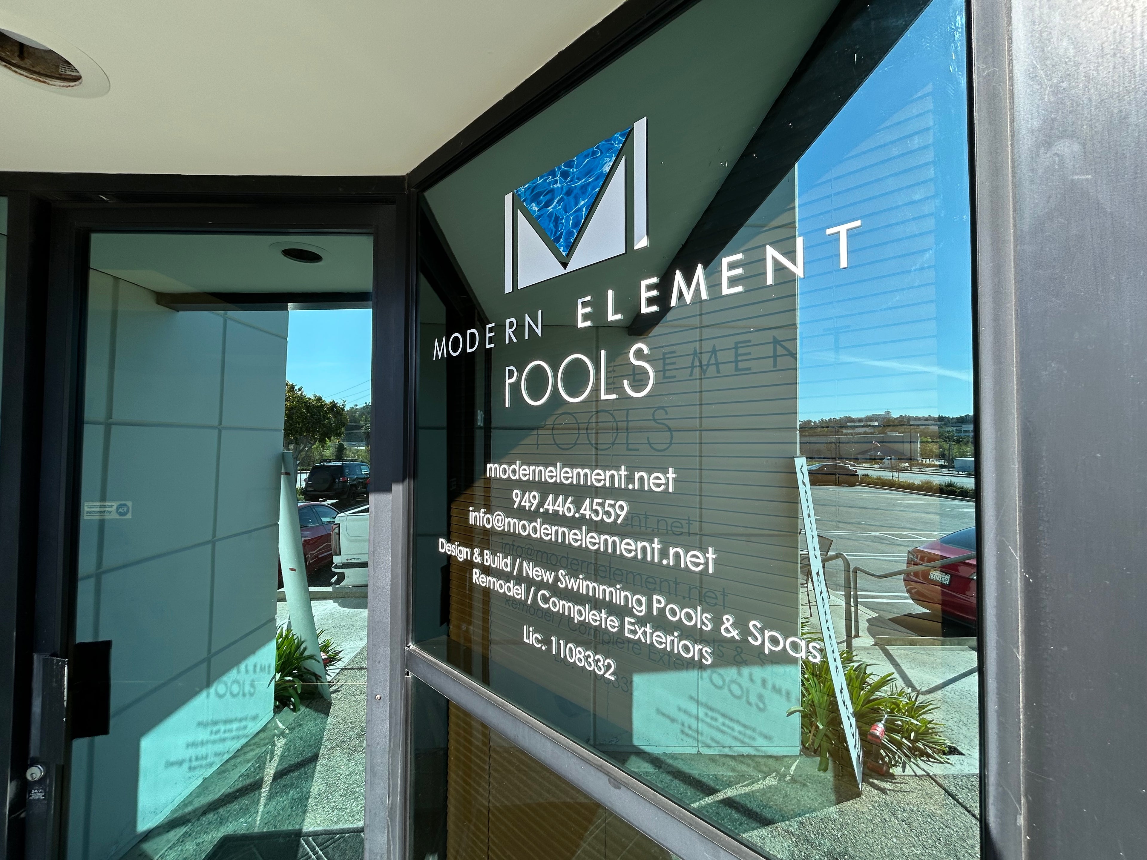 Modern Element Pools sign on a glass door with contact information.